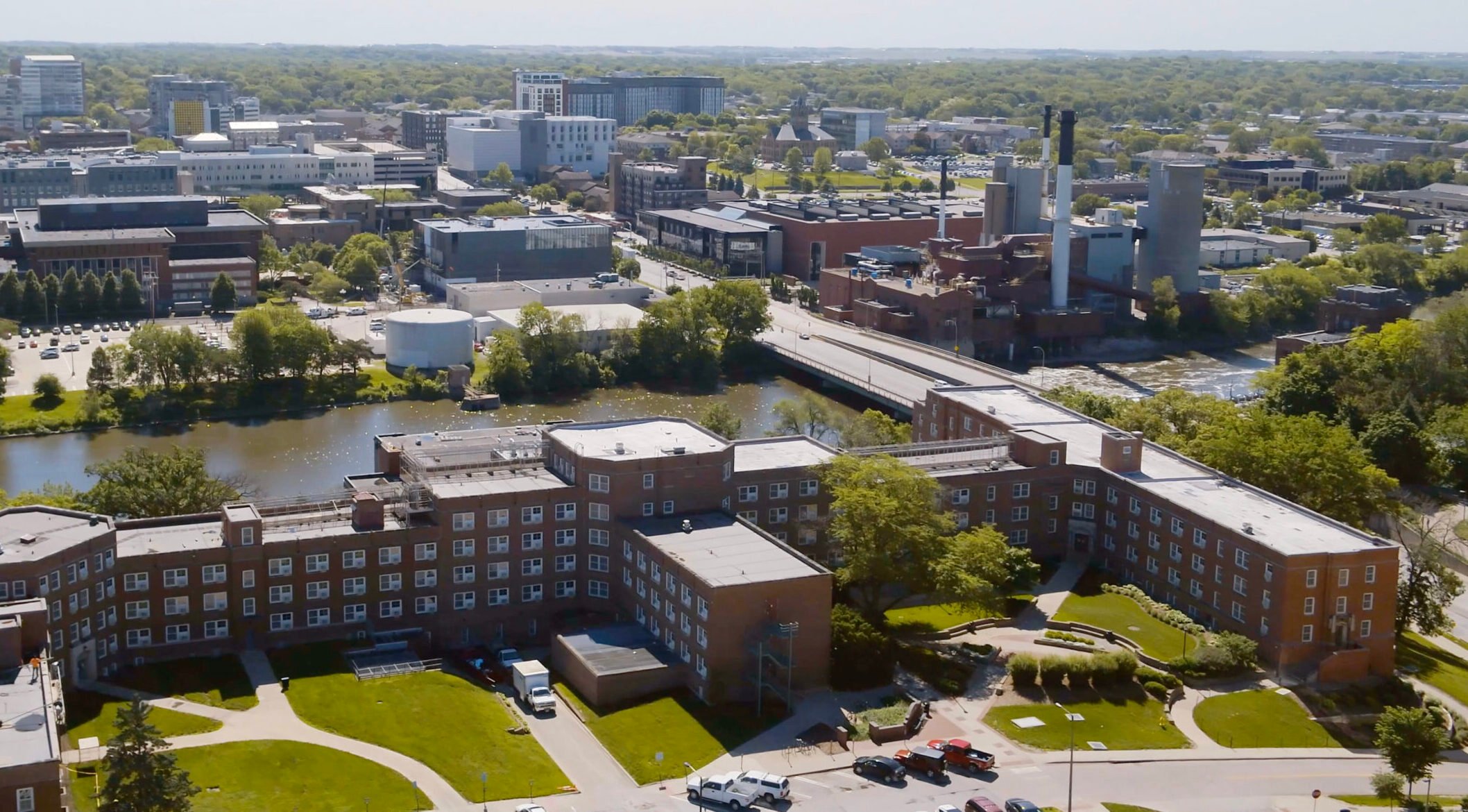 Aerial view of the Burlington Street Bridge spanning the Iowa River in downtown Iowa City, with the University of Iowa and downtown district visible in the background.