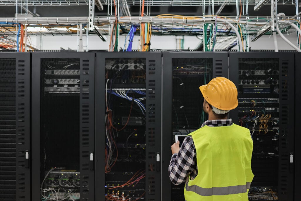 Young technician man working with tablet inside big data center room full of rack servers - Focus on man head